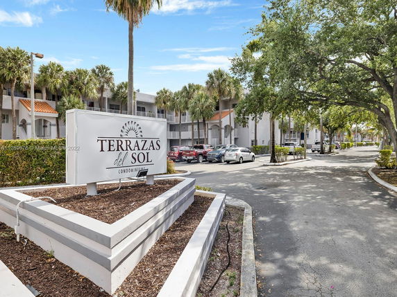 Front view of Terrazas del Sol condominium complex with trees and parked cars.