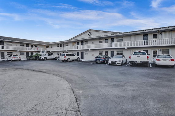 Outdoor parking area in front of a two-story building with multiple parked cars.