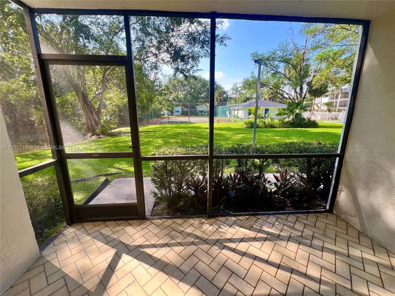 View of a grassy area with trees and a nearby building seen from a screened patio.