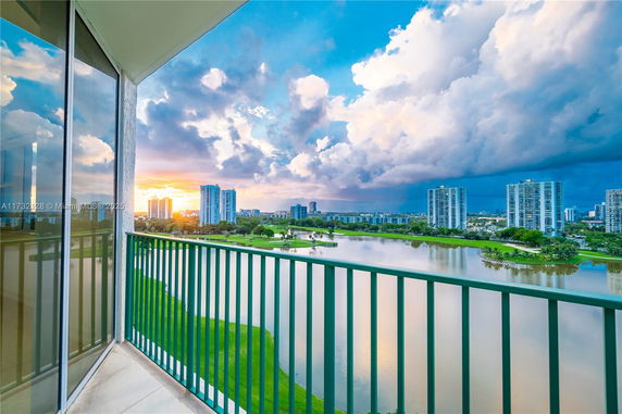 View from a balcony overlooking a cityscape with buildings and a body of water at sunset.