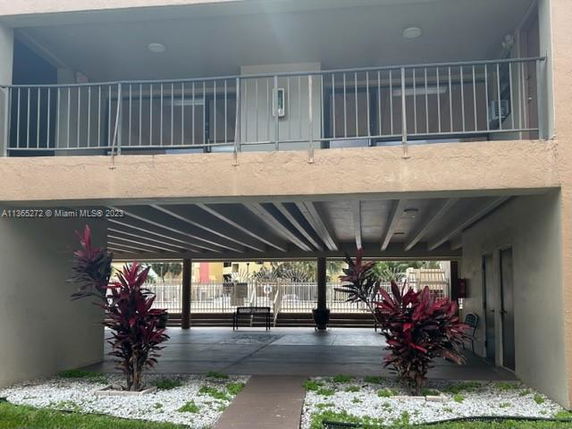 Covered parking area beneath a building with upper-floor balconies and potted plants.