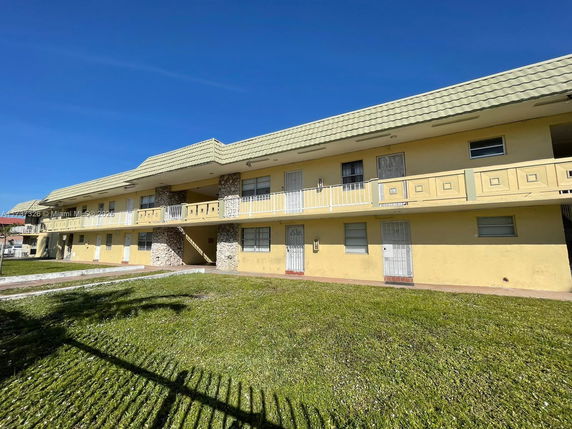 Front view of a two-story building with a yellow facade and balcony.