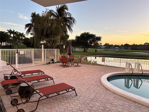 Outdoor area with a swimming pool, lounge chairs, and a dining table overlooking a golf course and water body.