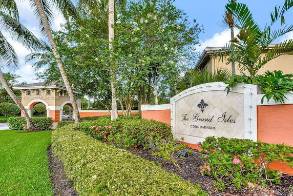Entrance sign for The Grand Isles Condominium surrounded by lush greenery.
