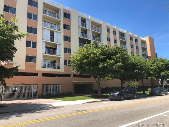 Front view of a multi-story residential building with balconies and ground-level parking.