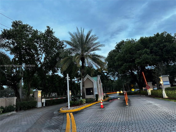 Front view of a small guardhouse at an entrance with palm trees and a barrier gate.