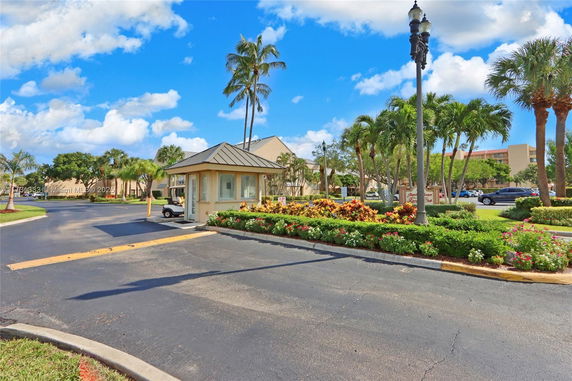 View of a security booth and landscaped entrance area with palm trees.