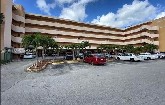 Outdoor parking area with multiple cars in front of a multi-story building.
