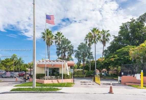 Entrance view of a gated community with a small guardhouse and American flag.