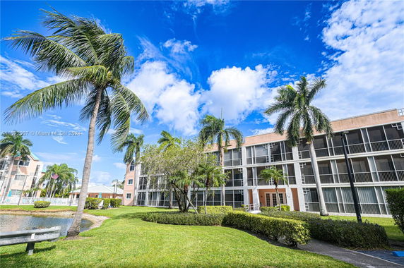 Multi-story apartment building surrounded by palm trees and green landscape.