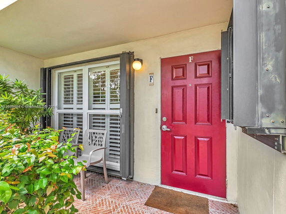 Front view of a building entrance with a red door and a small outdoor seating area.