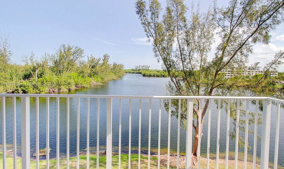 Panoramic view of a water body with trees and distant buildings, seen from a balcony.