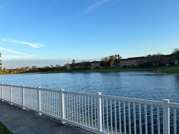 View of a waterbody with houses along the shore and a white fence in the foreground.