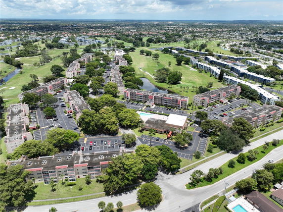 Aerial view of a suburban area with multiple apartment buildings, parking lots, greenery, and roads.