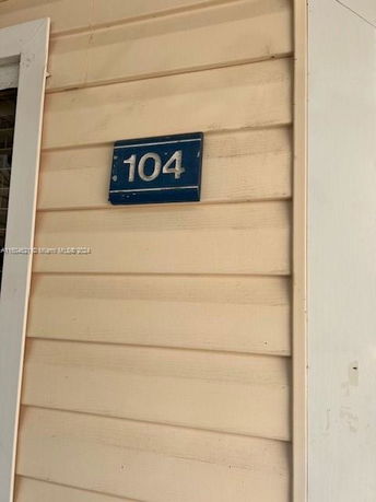 Section of a building exterior with a blue house number sign displaying 104.