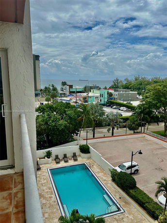 Panoramic view from a building showing a swimming pool, parking area, and nearby ocean.