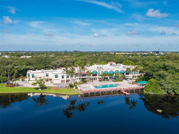 Aerial view of a large estate with a swimming pool adjacent to a body of water, surrounded by greenery and trees.