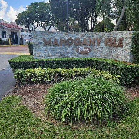 Front view of an entry sign for Mahogany Isle with a small building in the background.