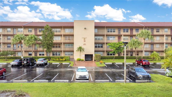 Front view of a multi-story building with a central entrance and adjacent parking area.