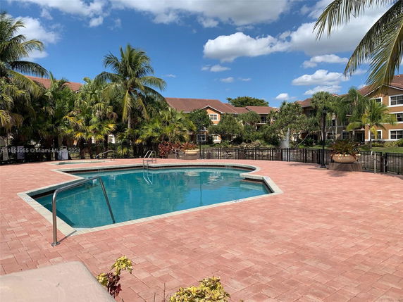 Outdoor swimming pool with surrounding palm trees and residential buildings in the background.