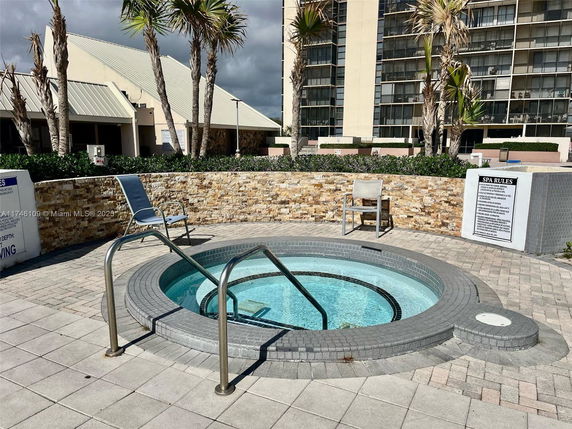 Outdoor spa area with a hot tub and surrounding chairs near a building.