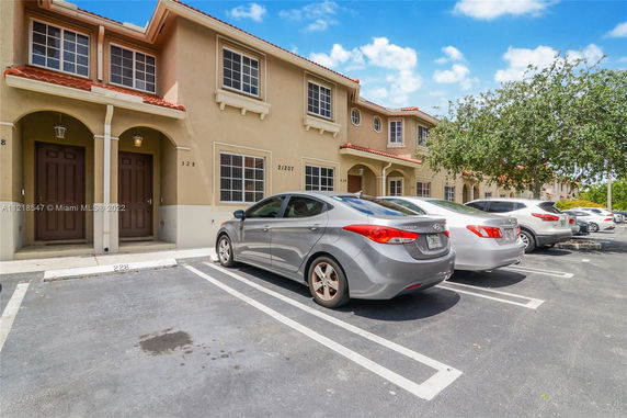 Outdoor parking area in front of a two-story townhouse with a row of parked cars.