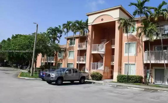 Front view of a multi-story apartment building with balconies and a parking area.