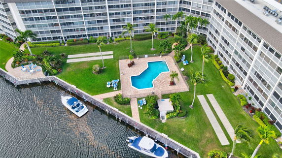 Aerial view of a swimming pool with surrounding landscaped garden next to an apartment building.