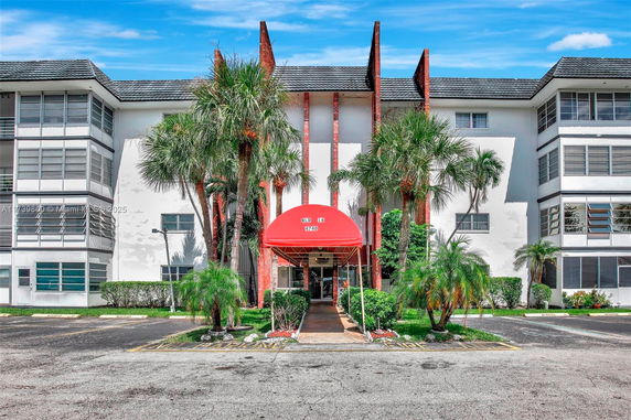 Front view of a multi-story building with a red awning and palm trees.
