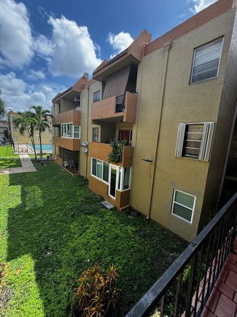 View of a multi-story residential building with balconies and a grass-covered area in front.