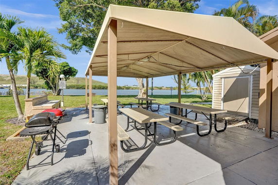 Outdoor area with picnic tables under a canopy near a body of water.
