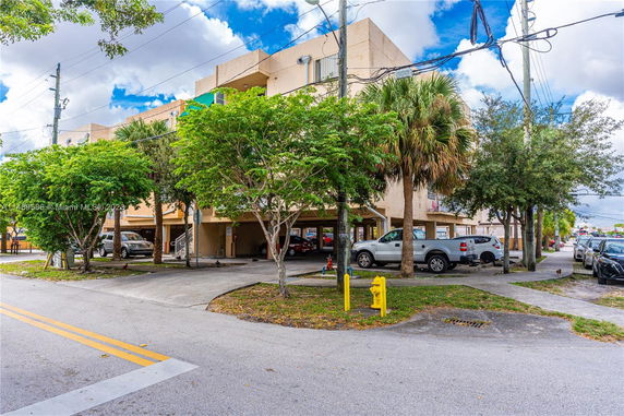 Outdoor parking area beneath a multi-story building with several vehicles parked.