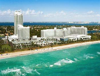 Aerial view of a large beachfront resort with multiple connected buildings, including a tall tower, situated near the ocean.