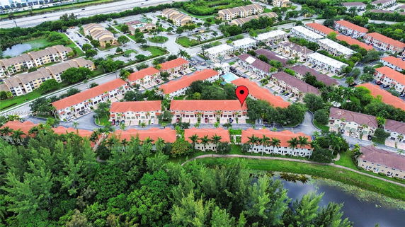 Aerial view of a residential area with multiple houses featuring red roofs surrounded by greenery and adjacent roads.