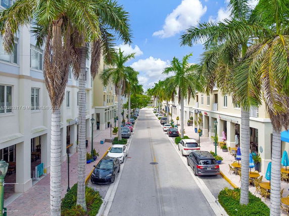 Street view lined with palm trees and buildings, with parked cars and outdoor seating.