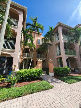 Front view of a multi-story residential building with balconies and tropical landscaping.