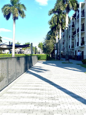 View of a multi-story building with palm trees and a paved walkway.