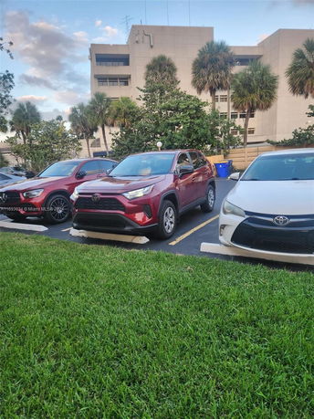 Outdoor parking area with several parked cars and a building in the background.