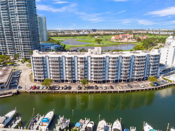 View of a multi-story waterfront building with a parking area and boats docked along the canal.