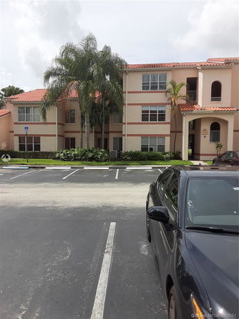Front view of a multi-story building with red-tiled roof and palm trees in front.