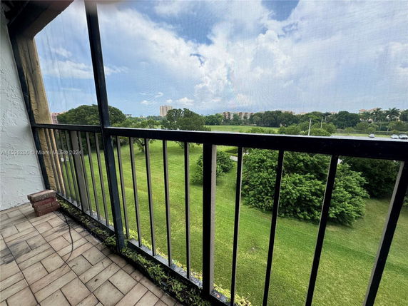 View from a balcony overlooking a green landscape with trees and distant buildings.