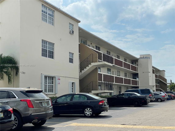Outdoor view of a multi-story residential building with a parking area in front.