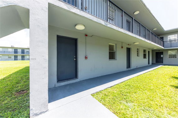 Exterior view of a multi-story building with a walkway and grass area.