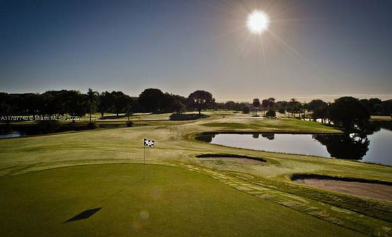 Golf course with a flag, sand traps, and a pond under a clear sky.