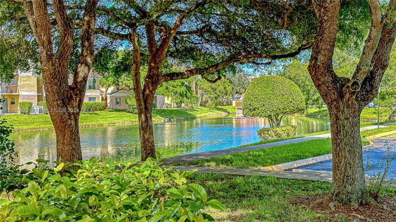 View of apartment buildings surrounding a pond with trees and landscaped greenery.