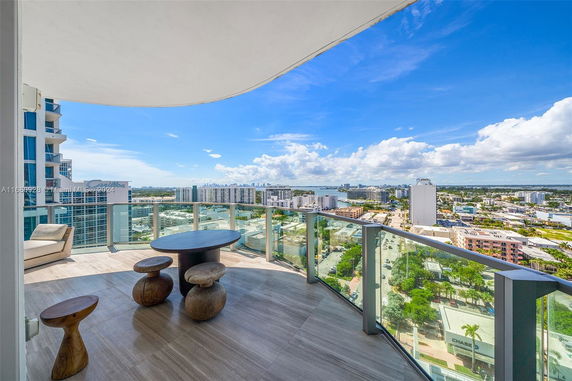Panoramic view from a high-rise balcony overlooking a cityscape and water.