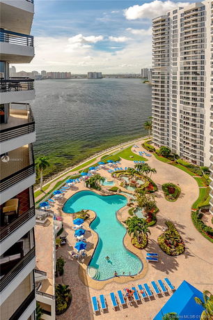 View from a building showcasing a swimming pool and adjacent high-rise structures beside a body of water.