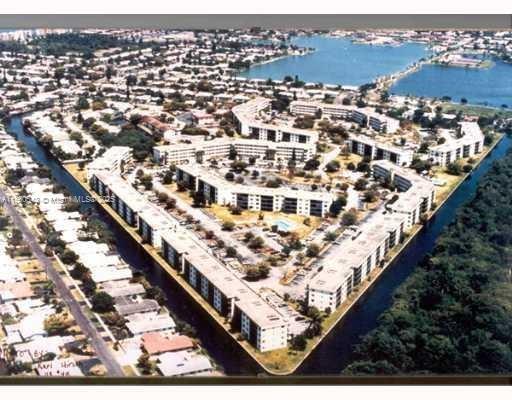 Aerial view of a large residential complex with multiple buildings surrounded by water canals and a cityscape in the background.