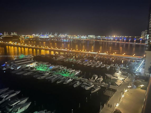 View of a marina with boats and city lights reflecting on the water at night.