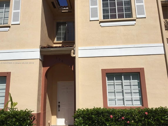 Front view of a townhouse with beige stucco walls and white shutters.
